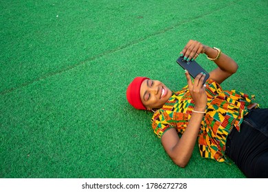 Beautiful African Lady Laying On The Floor In A Park Using Her Mobile Phone