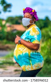 Beautiful African mother pregnant,colorfully dressed,expecting a baby,wearing face mask for protection in covid-19 pandemic - concept on Black maternity,obstetrics and gynecology