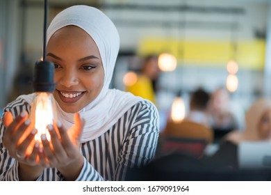 Beautiful african muslim woman holds modern lamp bulb with smiling happy expression, idea concept with selective focus.