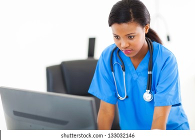 Beautiful African Nurse Looking At Computer Screen In Office