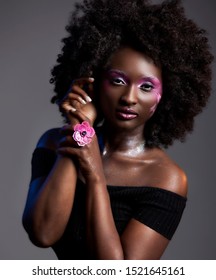 Beautiful African Woman With Big Curly  Afro And Flowers In Her Hair. The Black Female Model Is Wearing The Pink Make-up Happily To Highlight Her Wonderful Dark Skin Care