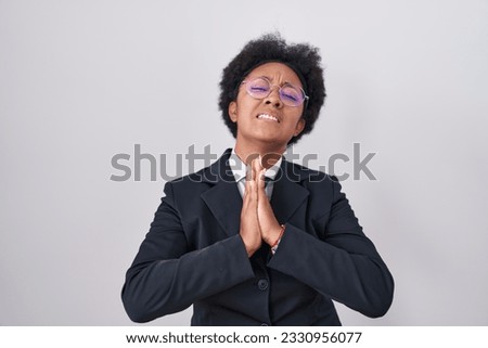 Beautiful african woman with curly hair wearing business jacket and glasses begging and praying with hands together with hope expression on face very emotional and worried. begging. 