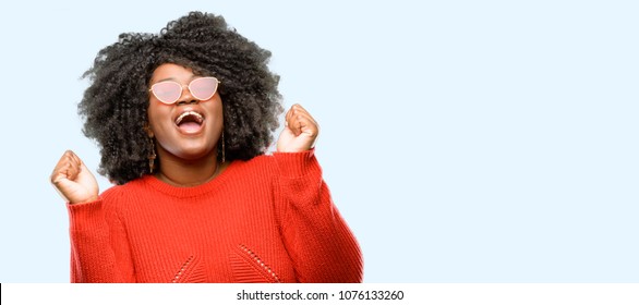 Beautiful african woman happy and excited expressing winning gesture. Successful and celebrating victory, triumphant, blue background