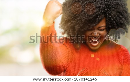 Beautiful african woman happy and excited expressing winning gesture. Successful and celebrating victory, triumphant, outdoor
