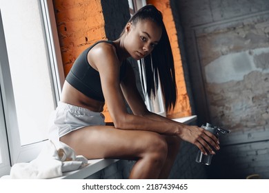 Beautiful African Woman Holding Bottle With Water While Sitting On The Window Sill In Gym