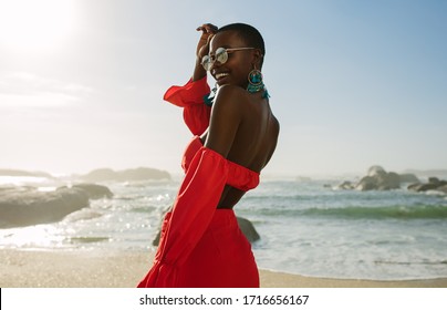 Beautiful african woman in red dress enjoying on the beach. Smiling female in beautiful dress walking along the shore.