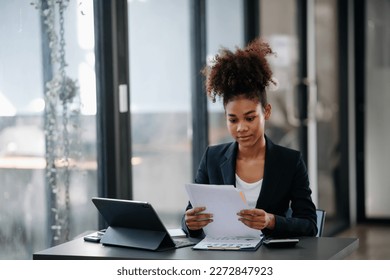  Beautiful African woman using laptop and tablet while sitting at her working place. Concentrated at work.