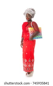 Beautiful African woman walking in traditional red clothing with bright wicker tote bag. Isolated on the white studio background