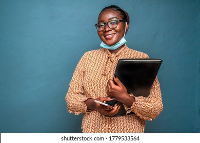 Beautiful African woman wearing spectacles, smiling, wearing surgical face mask for protection in covid-19 pandemic and holding a black case for documents and laptop,isolated on a blue background - Powered by Shutterstock