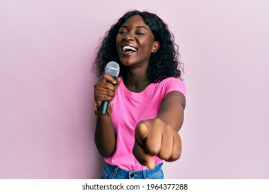 Beautiful African Young Woman Singing Song Using Microphone Pointing To Camera Smiling And Laughing Hard Out Loud Because Funny Crazy Joke. 