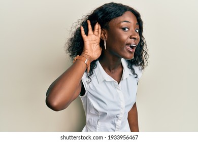 Beautiful African Young Woman Wearing Casual Clothes Smiling With Hand Over Ear Listening And Hearing To Rumor Or Gossip. Deafness Concept. 