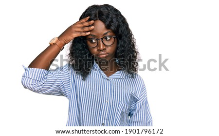 Beautiful african young woman wearing casual clothes and glasses worried and stressed about a problem with hand on forehead, nervous and anxious for crisis 