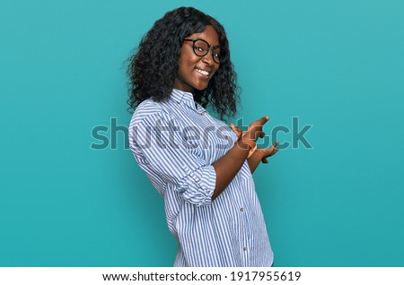 Beautiful african young woman wearing casual clothes and glasses inviting to enter smiling natural with open hand 
