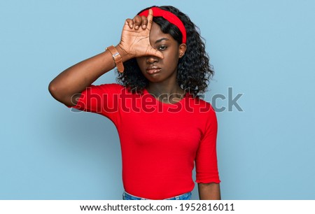 Beautiful african young woman wearing casual clothes making fun of people with fingers on forehead doing loser gesture mocking and insulting. 