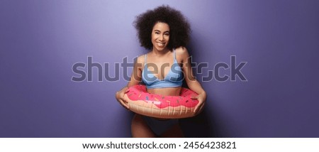 Beautiful African-American woman in bikini and with inflatable ring on purple background