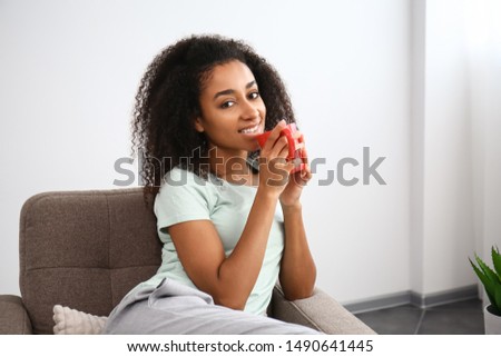 Beautiful African-American woman drinking tea in armchair at home