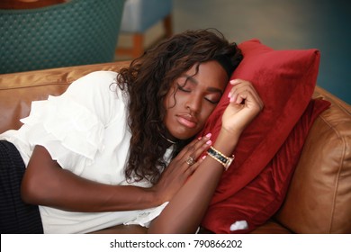 Beautiful African-American woman keeping head on red pillows while taking nap on comfortable sofa.  - Powered by Shutterstock