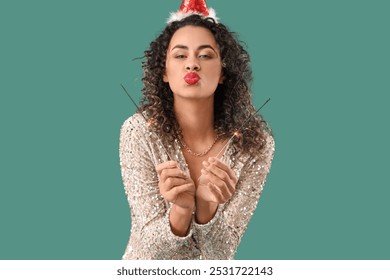 Beautiful African-American woman in Santa hat with sparklers blowing kiss on green background. New Year celebration - Powered by Shutterstock