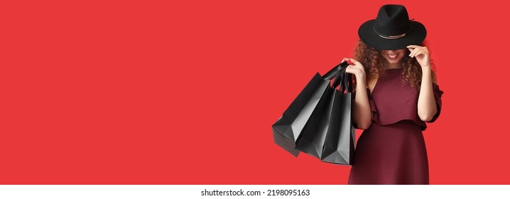 Beautiful African-American woman with shopping bags on red background with space for text. Black Friday sale
