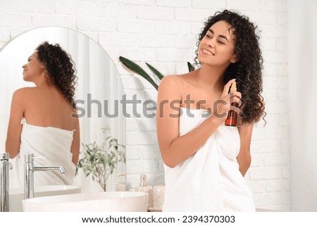 Beautiful African-American woman spraying hair in bathroom
