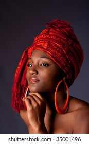 Beautiful African-American woman wearing a traditional tribal red orange head scarf and big orange hoop earrings, supporting her chin with hand, isolated.