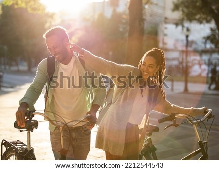 Beautiful afro american couple with big smiles on their face pushing their bikes through the city and having fun