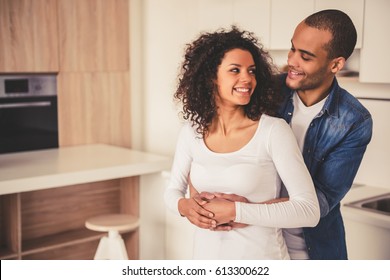 Beautiful Afro American couple is hugging, looking at each other and smiling while standing in kitchen