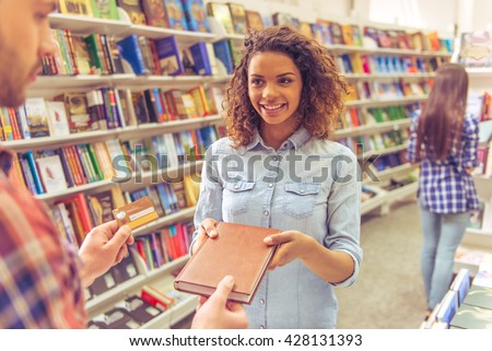 Beautiful afro american girl is smiling while buying book at the bookshop using a credit card