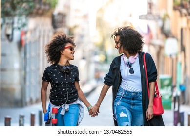 Beautiful Afro Young Mother Hanging out with her Daughter Outdoors. Mother or Sister Walking Together ,Holding Hands and Smiling in the Street. Lifestyle Concept. - Powered by Shutterstock