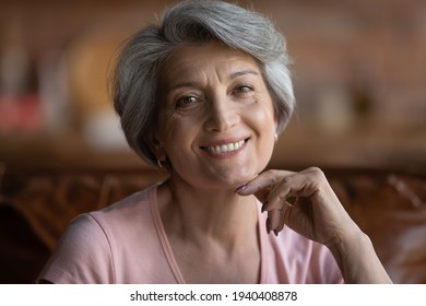 Beautiful age. Headshot portrait of happy mature latin female pensioner looking at camera with white smile. Attractive grey haired 60s retired hispanic woman posing indoors touching chin with finger