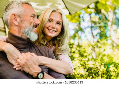 Beautiful aged blond woman hugging her grey-haired husband in park