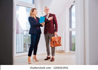 Beautiful Agent. Stylish Beautiful Estate Agent Wearing Blue Costume Talking To Her Client While Standing In Fancy Apartment