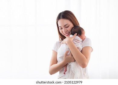 Beautiful Aisan Mother Holding And Embrace Newborn Baby In Her Arms. Woman Holding Adorable Infant In Arms And Support Baby Back By Her Hand. Mom And Son Spend Time Together In White Room.