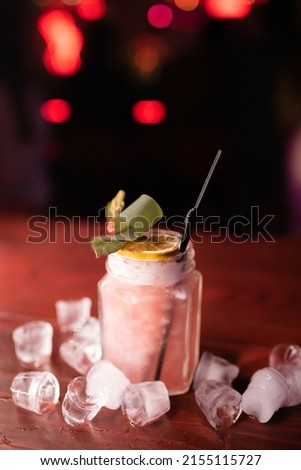 Beautiful alcoholic cocktail on a wooden counter in a nightclub. Garnished with fruits and ice