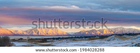 Beautiful alpenglow view of Mount Timpanogos Wasatch mountains at Saratoga Springs, Utah. There is a snowy field and houses against the lake and mountain view with pink orange reflection at the back.