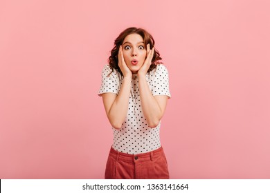 Beautiful amazed girl in t-shirt looking at camera. Studio shot of charming surprised lady isolated on pink background.