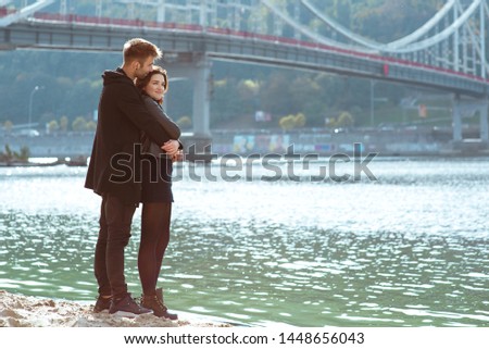beautiful amazing funny cheerful young couple (man and woman) hugging outdoor by the river on bridge background. Girlfriend and boyfriend. Family, love and friendship concept