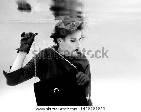 beautiful amazing stylish pretty young woman in green dress, red gloves, black clutch bag and tights in the net underwater in the swimming pool. Fashion and shopping concept