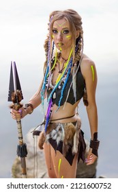 Beautiful Amazon Woman In A Fur Medieval Costume, In War Paint, In The Jungle With A Spear Against The Background Of The River.