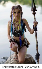 Beautiful Amazon Woman In A Fur Medieval Costume, In War Paint, In The Jungle With A Spear Against The Background Of The River.