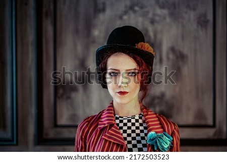 A beautiful animator or cabaret girl in a costume of a ringmaster (entertainer) of an old circus: a red striped tailcoat, a bowler hat, a large buttonhole on her chest. Vintage steampunk style