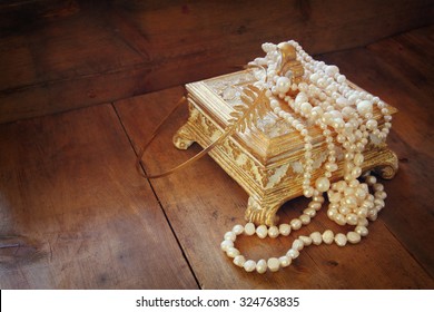 A beautiful antique golden jewelry box with natural white pearls on wooden table. retro filtered image
