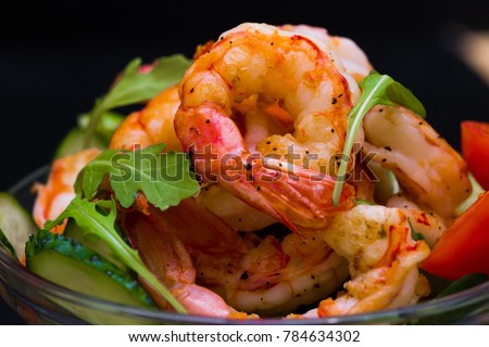 Beautiful appetizer langoustines salad, decorated vegetables cucumber and rukola.  Black background. Close up. Fried shrimps. 