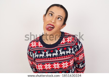 Beautiful arab girl wearing christmas sweater over isolated white background showing grimace face crossing eyes and showing tongue. Being funny and crazy