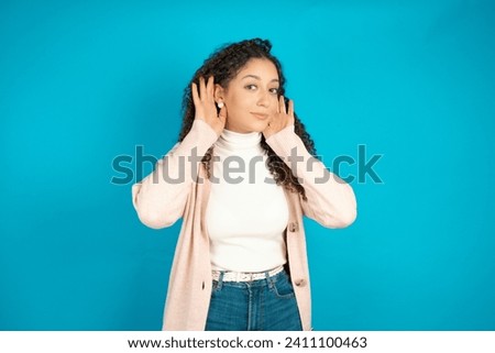 Beautiful arab teen girl with curly hair wearing turtleneck sweater Trying to hear both hands on ear gesture, curious for gossip. Hearing problem, deaf