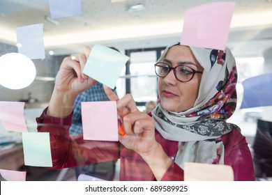 Beautiful Arab Woman Wearing Hijab Putting Sticky Notes On Glass In Modern Office. 