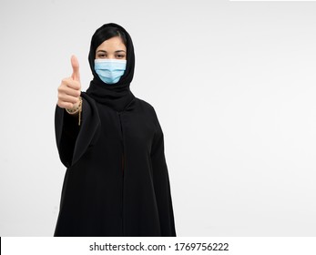 Beautiful Arab young woman with disposable face mask. Protection versus viruses and infection. Studio portrait, concept with white background. Arabic Woman showing thumb up. - Powered by Shutterstock