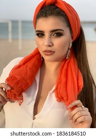 Beautiful Arabian woman with bright makeup golden jewelry and orange scarf on hair, outdoors fashion portrait