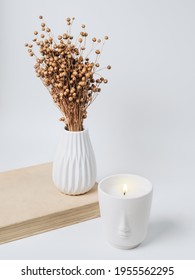 A beautiful arrangement of dried flowers in a stylish ceramic vase and a candle in a white candlestick. A bouquet of dry flax on a light background. Minimal modern interior decoration.