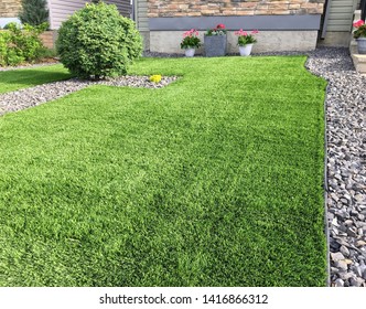 A beautiful artificial lawn in the front yard with nice flowers and shrubs surrounding it